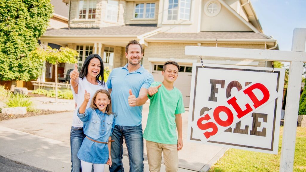 Family happily stand in front of their home with a sold sign